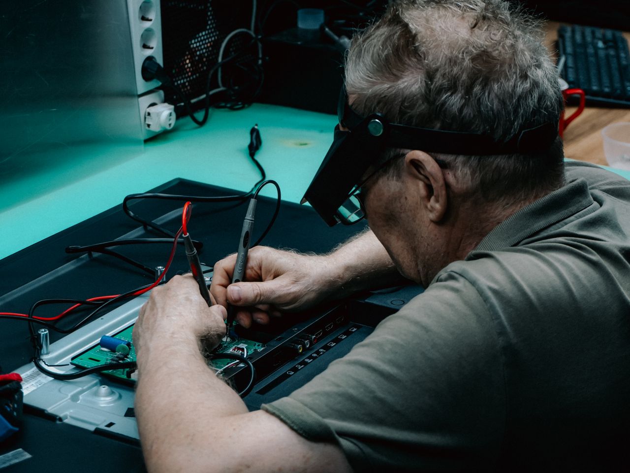 Senior technician soldering a circuit board with precision tools in a workshop.